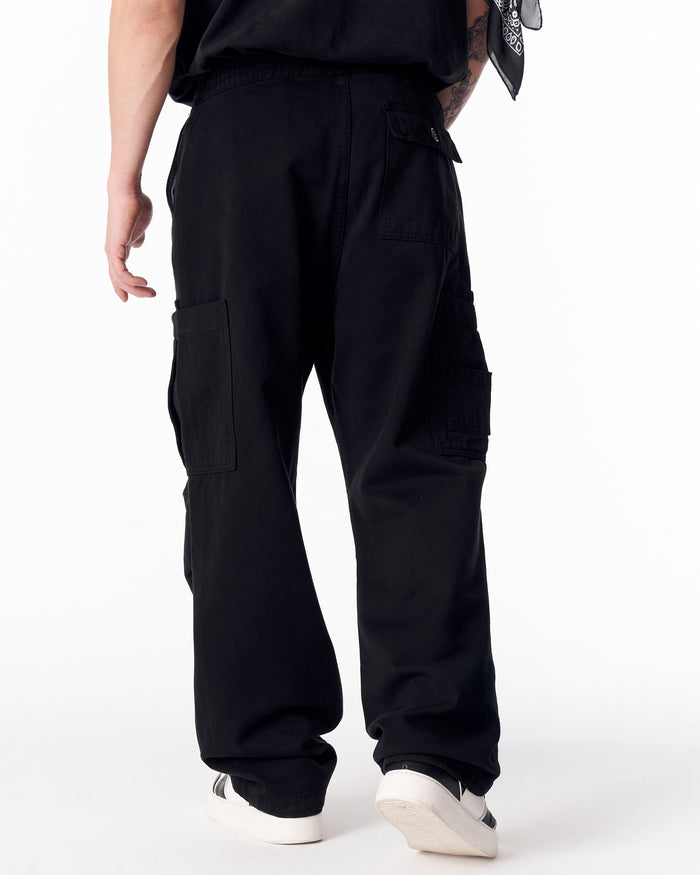 Martin Valen men's oversize black cargo jogger pants, side view highlighting thigh cargo pocket with hand in pocket